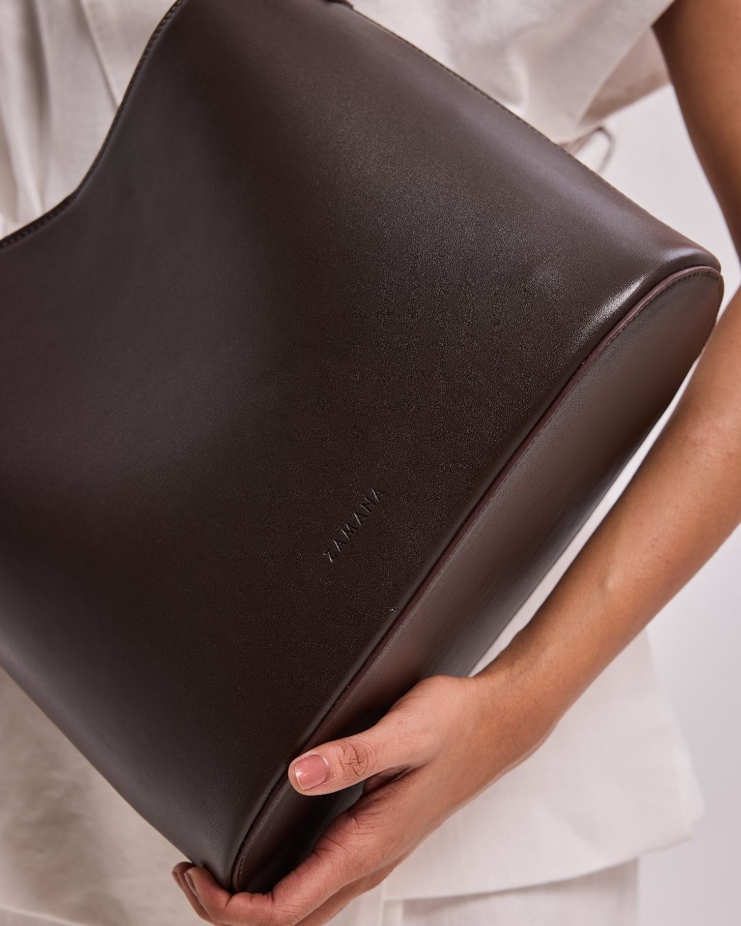 THE DECEMBER dark brown leather shoulder bag, close-up of front panel and logo
