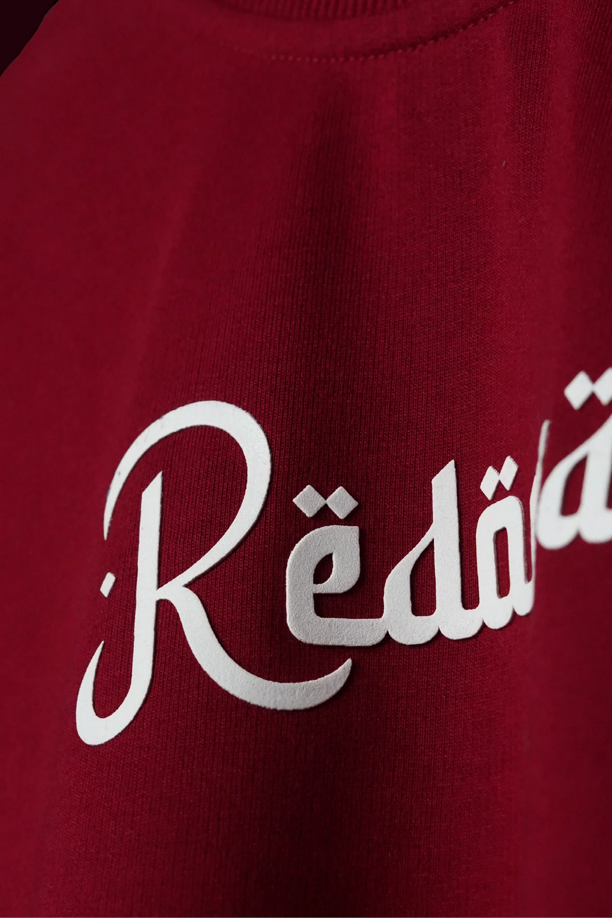 Crimson red T-shirt close-up of white Arabic script across the chest