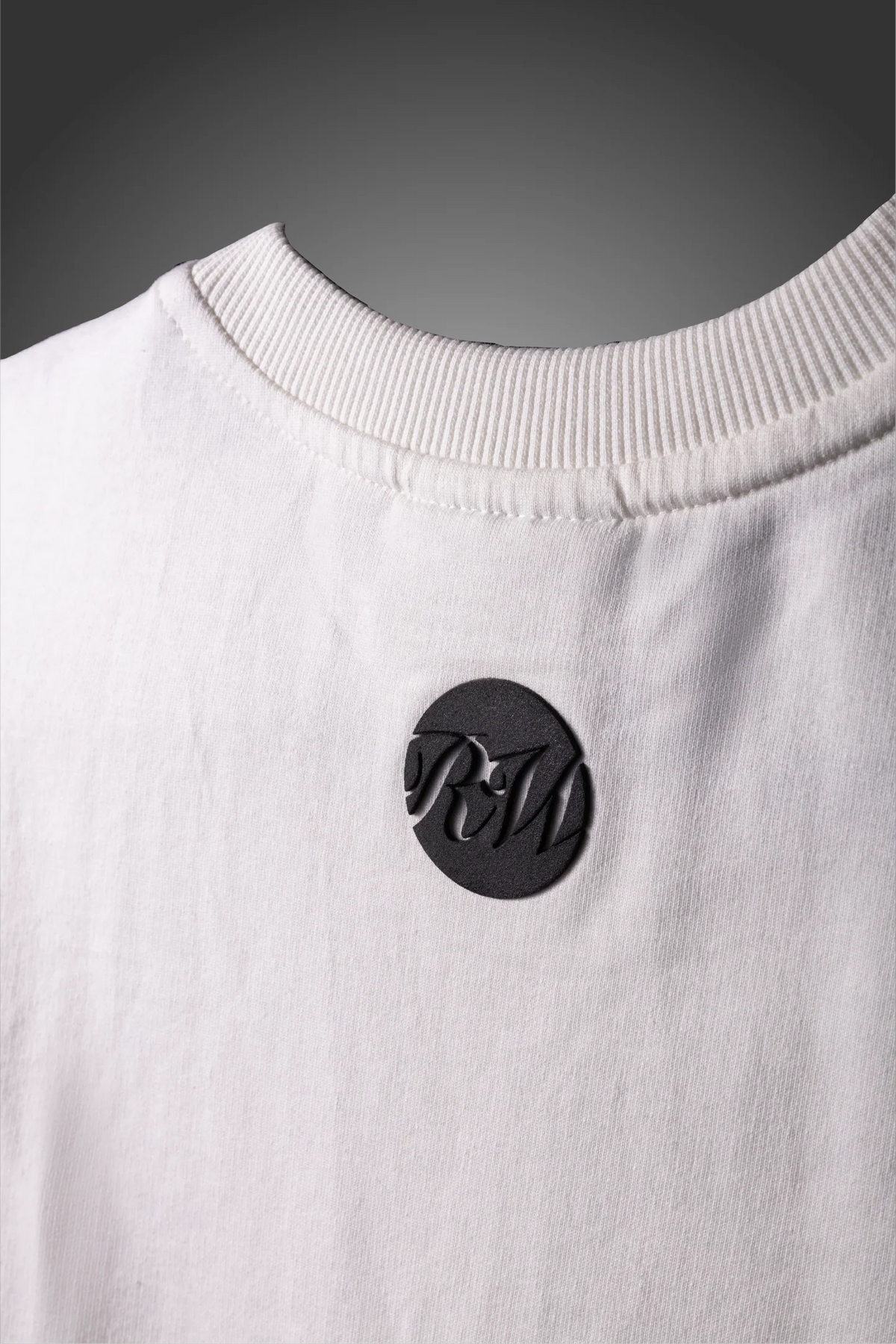 White crew-neck T-shirt with black circular logo patch on the chest