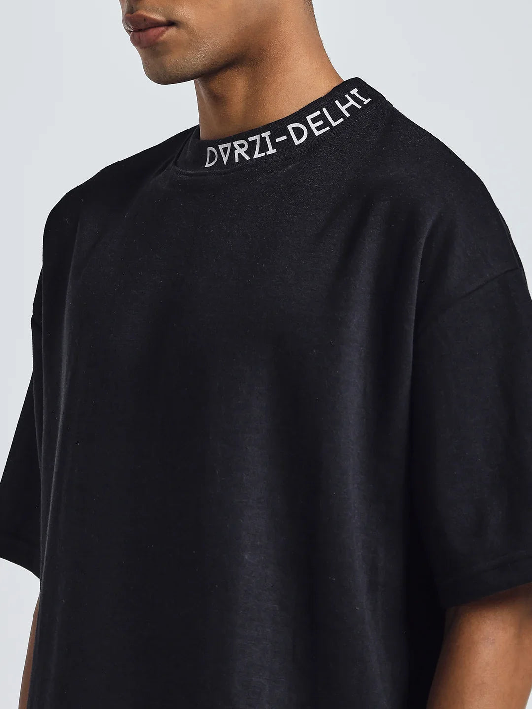 Black deconstruction T-shirt close-up: neck print reading "DVZR1-DELHI".