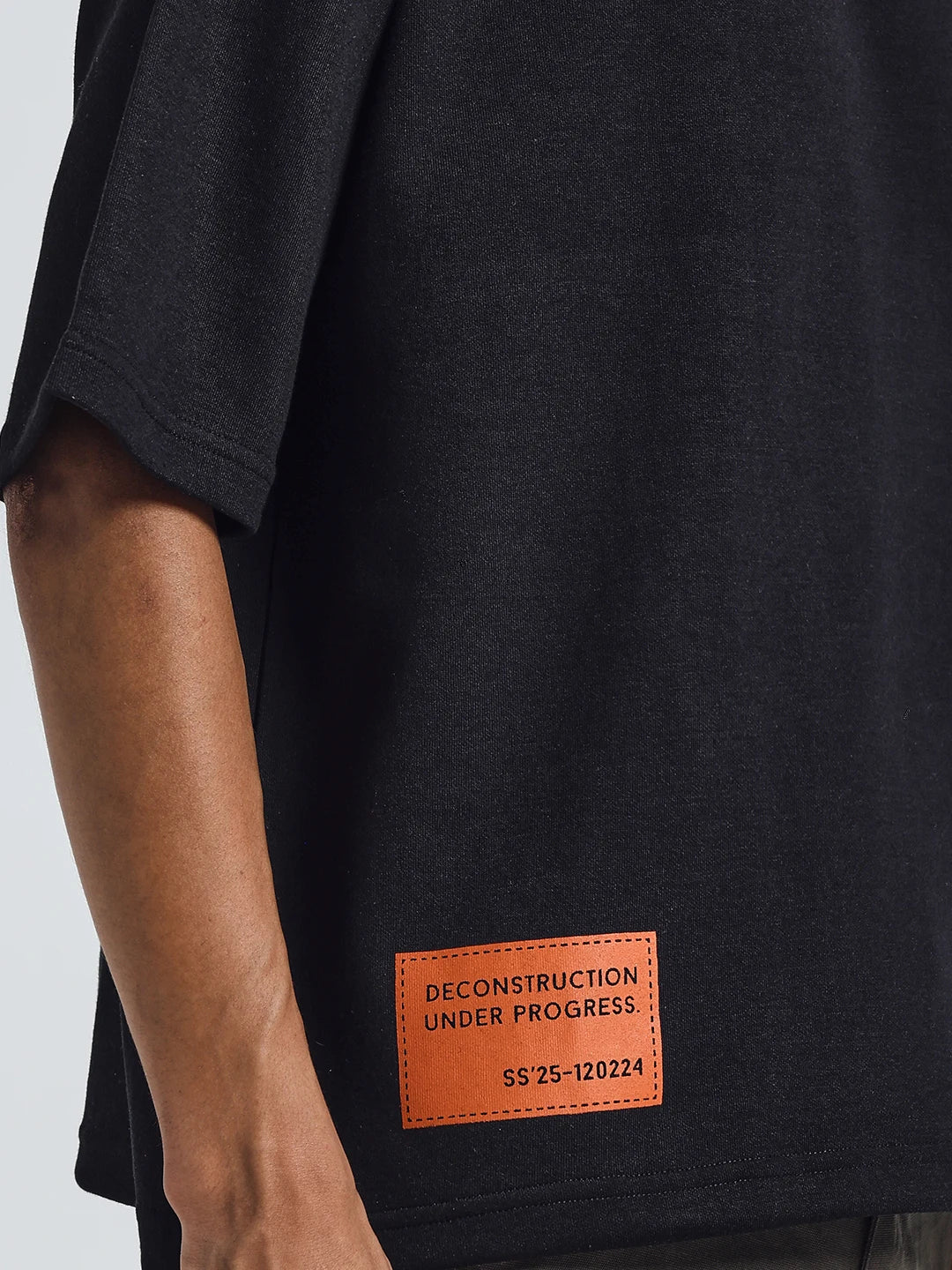 Close-up of black deconstruction T-shirt: orange rectangular label at lower front.