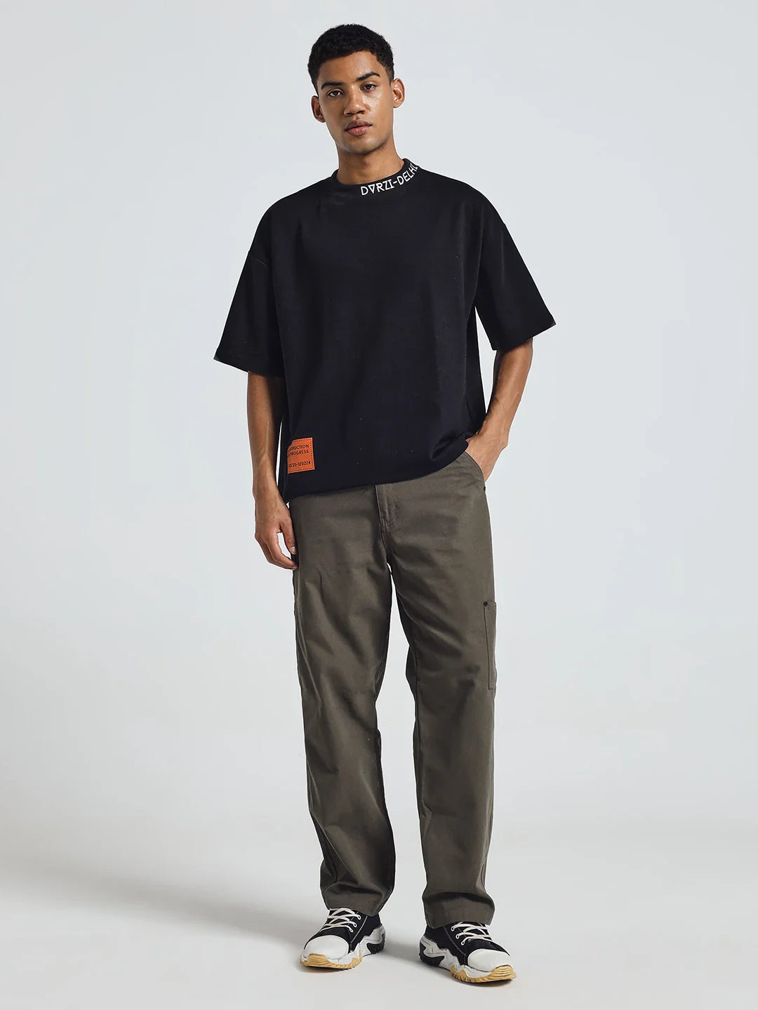 Black deconstruction T-shirt with crew neck and orange label at lower front, with olive pants.