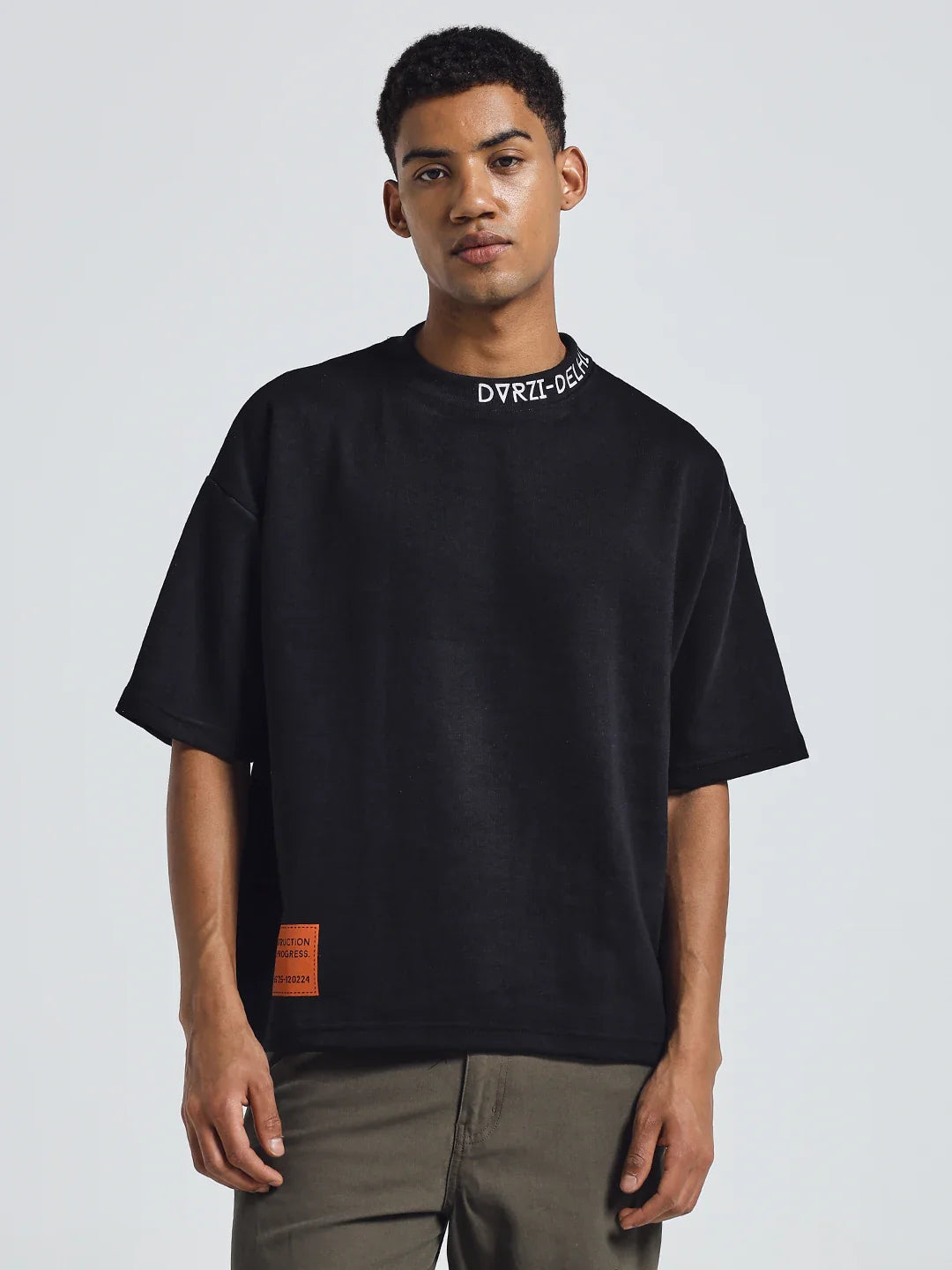 Black deconstruction T-shirt with crew neck and orange label patch at left hem.