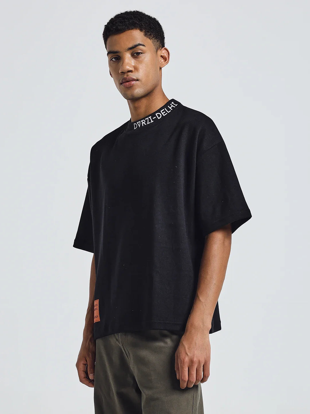 Black deconstruction T-shirt with crew neck and orange side label, worn with olive pants.