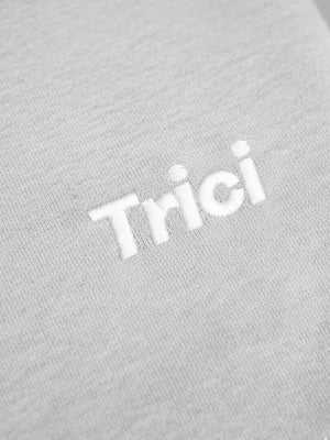 Grey melange hoodie fabric close-up with white 'Trici' printed logo