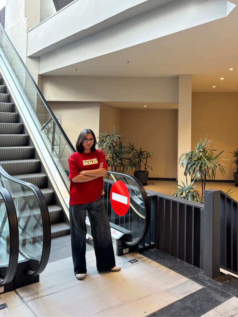 Red graphic T-shirt worn with jeans; front text “RETIRED DRUG DEALER” visible