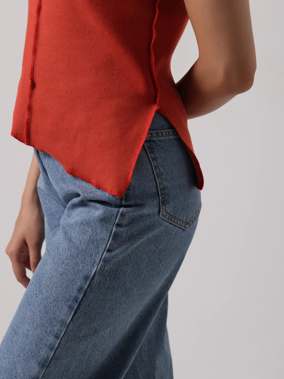 Red cap-sleeve top close-up: exposed front seam, curved hem, and side vent