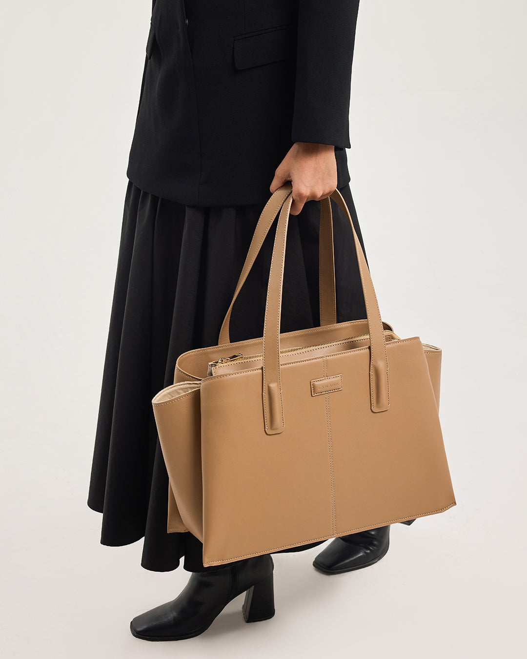 Caramel leather tote bag held by model with top handles and metal hardware