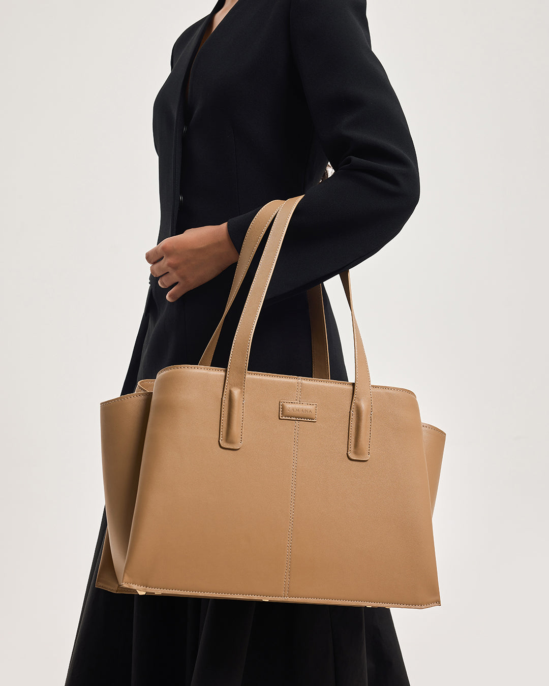 Caramel leather tote bag on model with two handles and front logo label