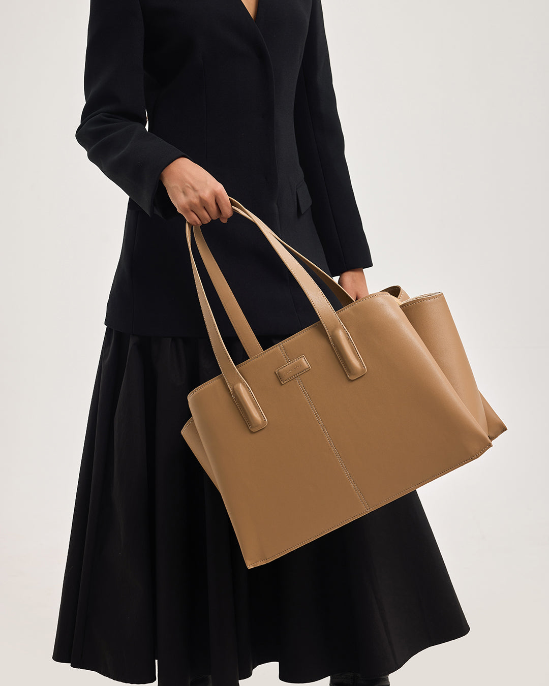 Caramel leather tote bag held low with structured shape and top handles
