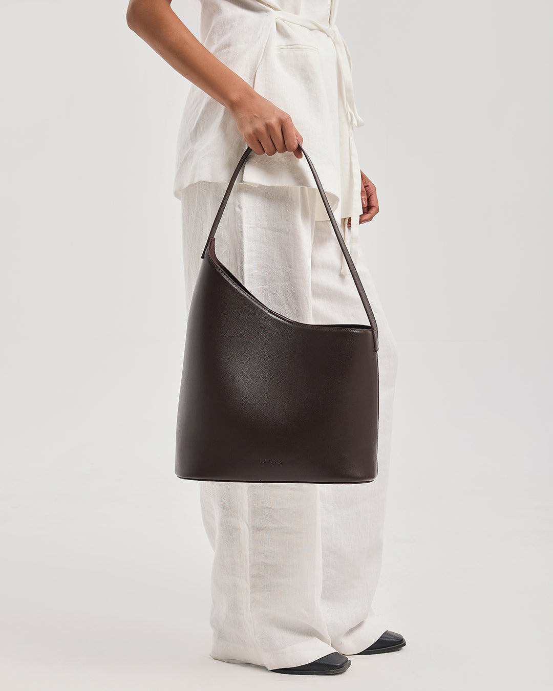 THE DECEMBER dark brown leather shoulder bag carried at side