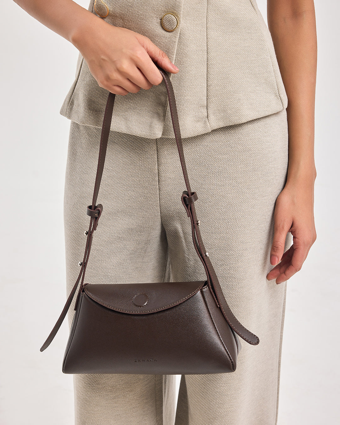 Dark brown leather shoulder bag held by model with curved flap front