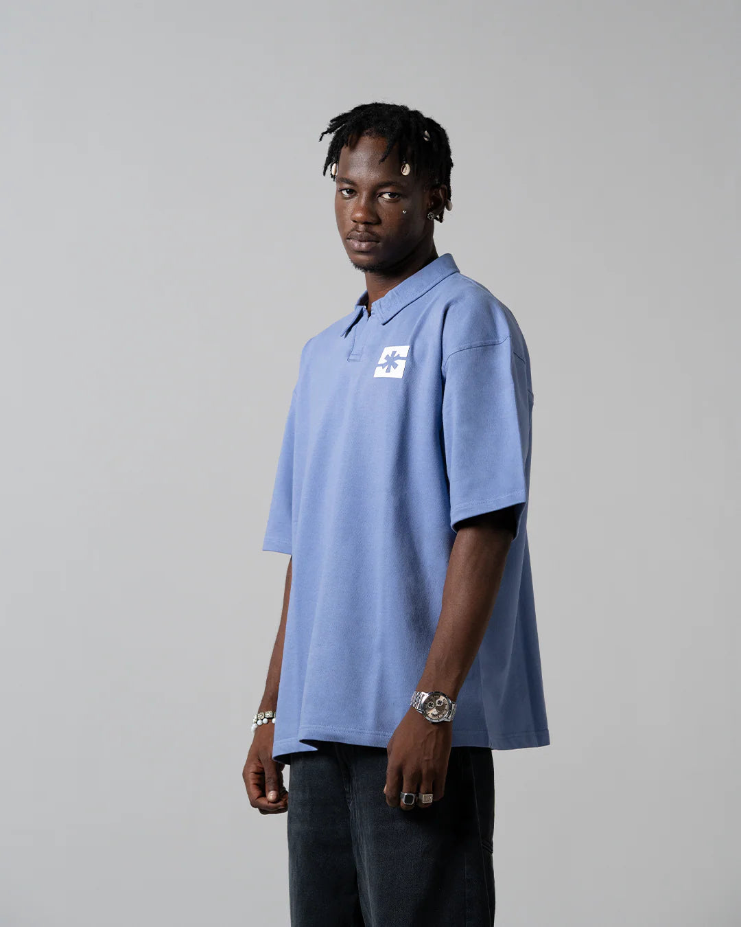 Light blue short-sleeve polo shirt with collar and chest logo patch, side view.