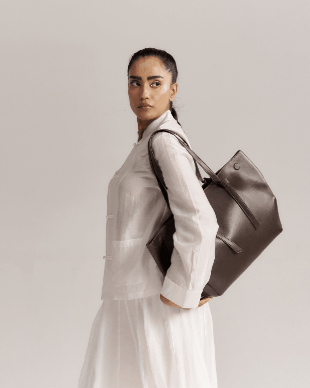 Brown leather tote bag with shoulder strap and bow-tie detail, side view