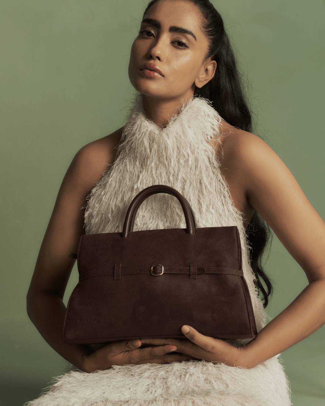 Dark brown handbag in hands with top handles and front buckle
