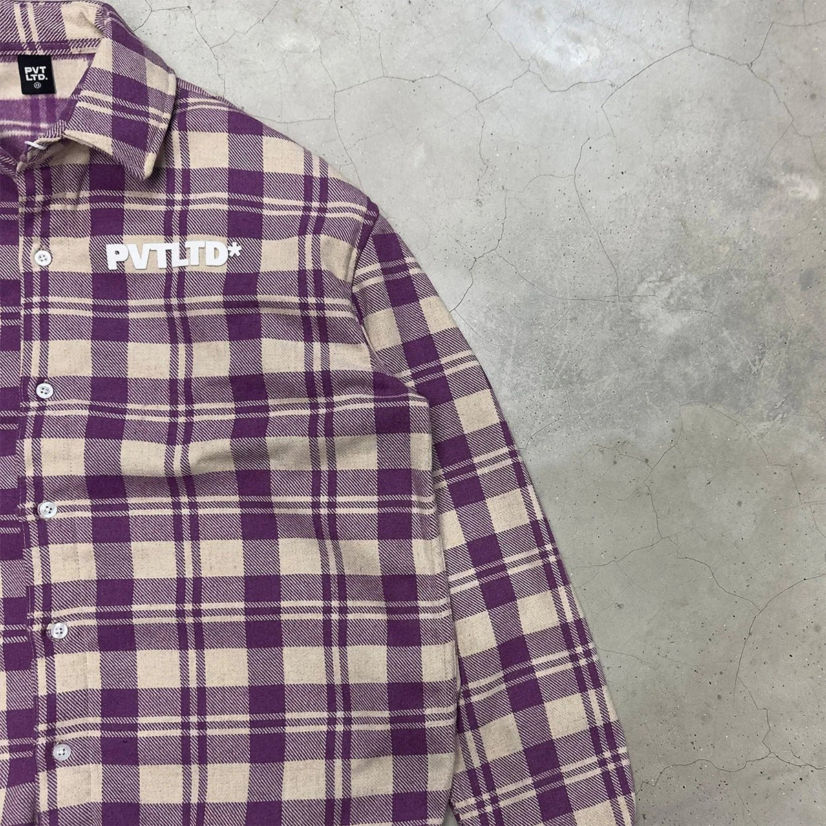 Close-up plaid shirt chest with PVTLTD* logo and button placket