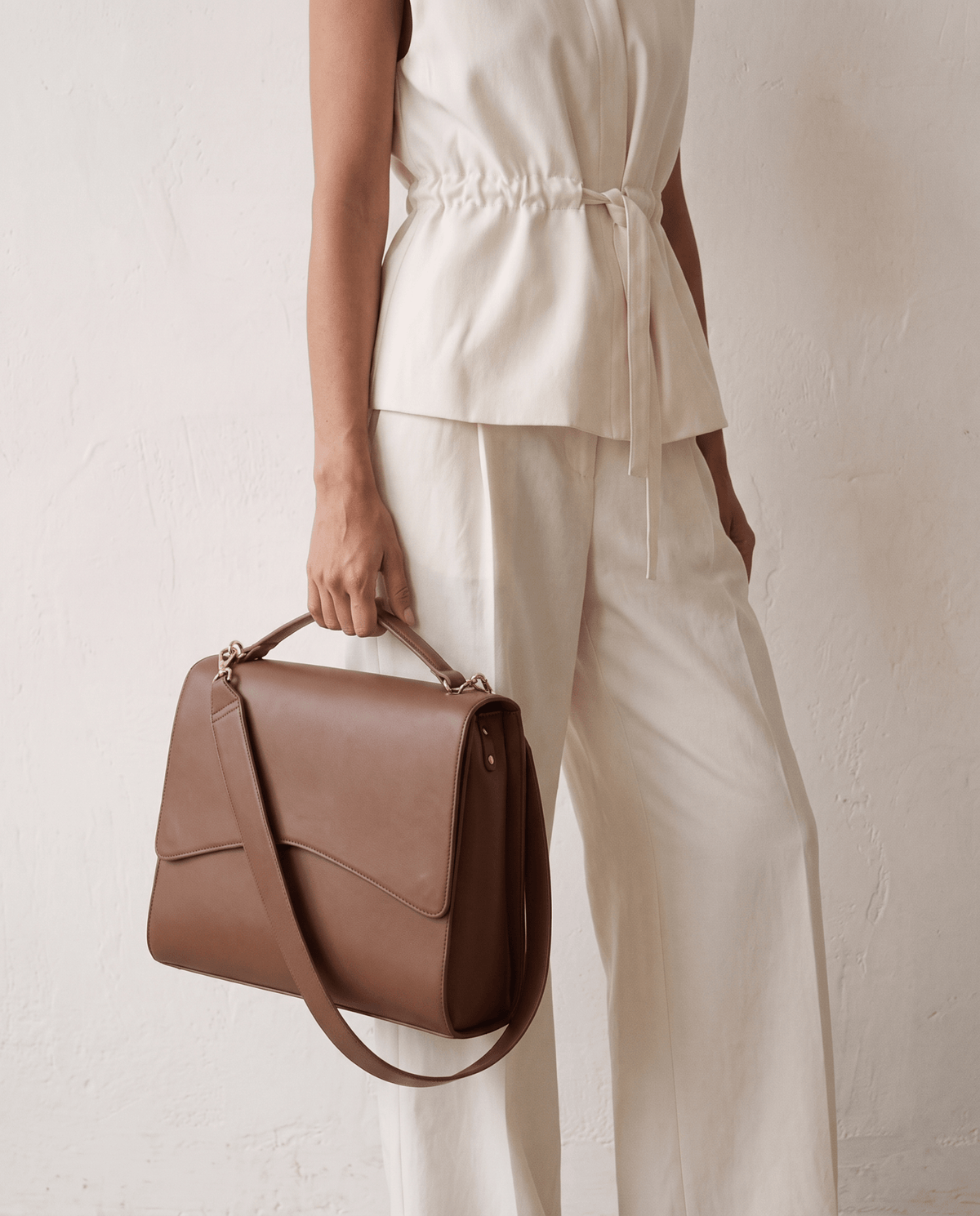 Person carrying light brown handbag with top handle and shoulder strap