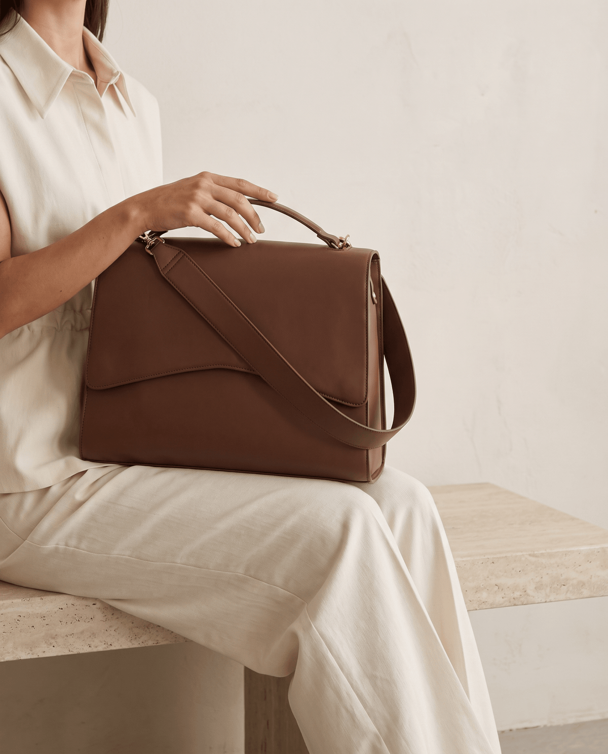 Light brown handbag being held on lap with top handle and crossbody strap
