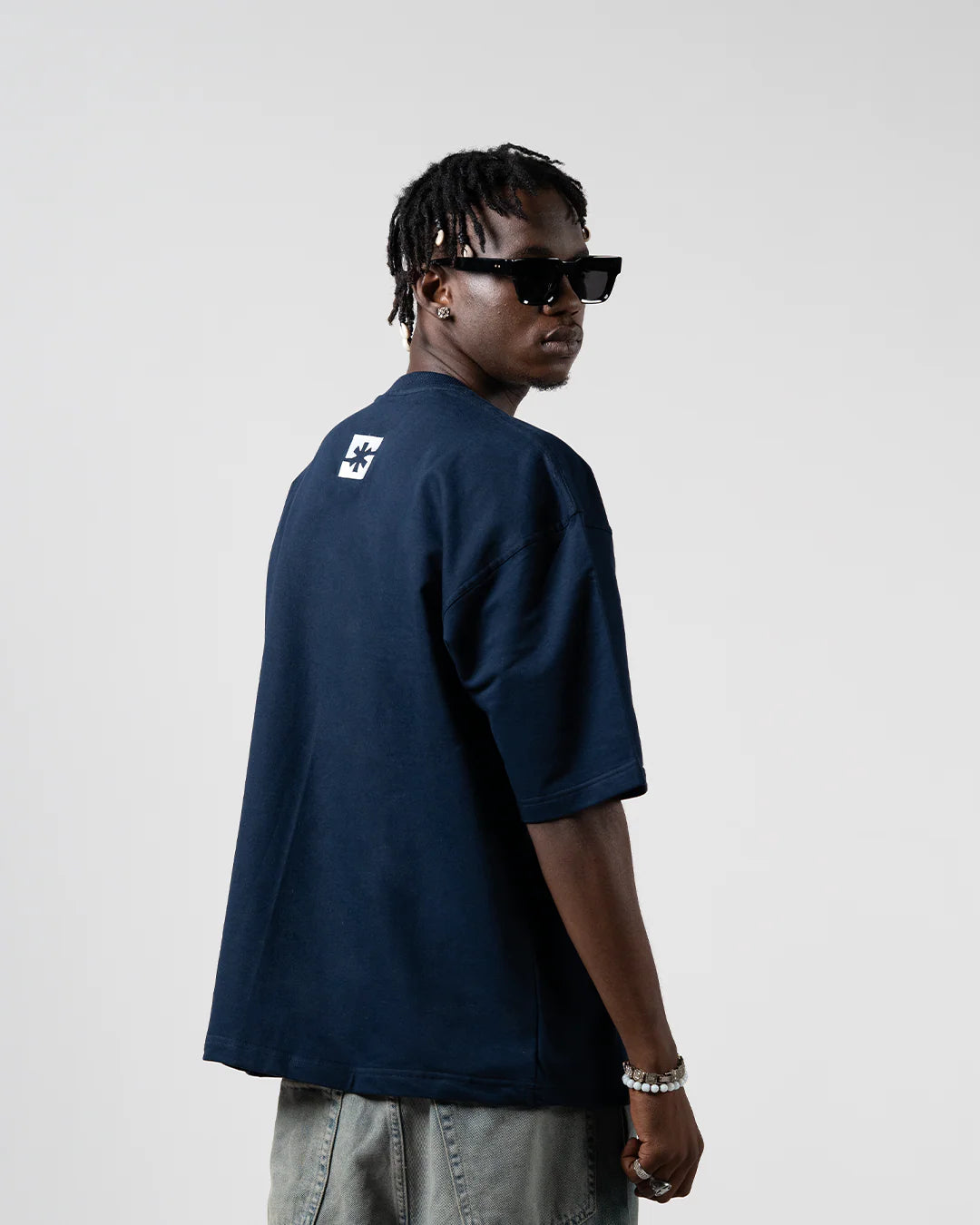 Dark blue crew-neck T-shirt shown from side, small square logo on back
