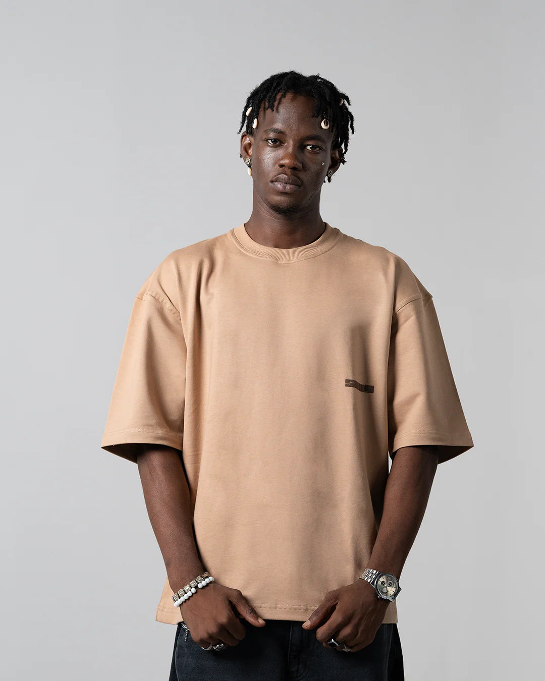 Beige crewneck T-shirt with small chest logo, short sleeves on model.