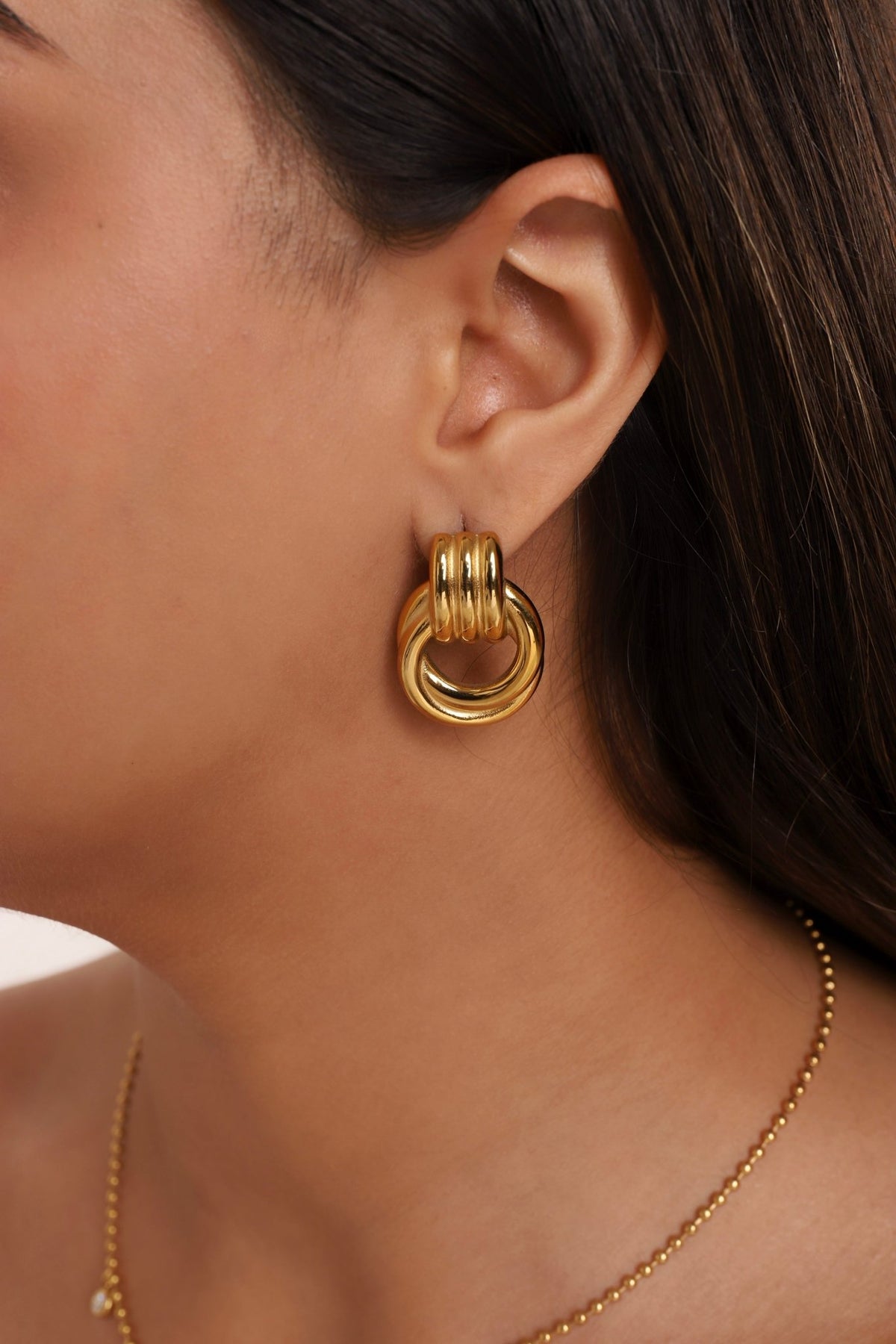 Gold-tone chunky layered hoop earrings with stacked coil bands, close-up on ear