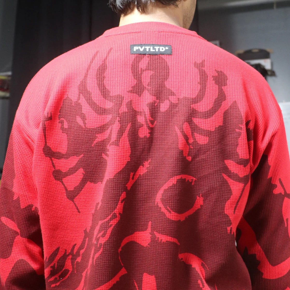 Red long-sleeve waffle knit top, back view, dark illustrated monster graphic and label