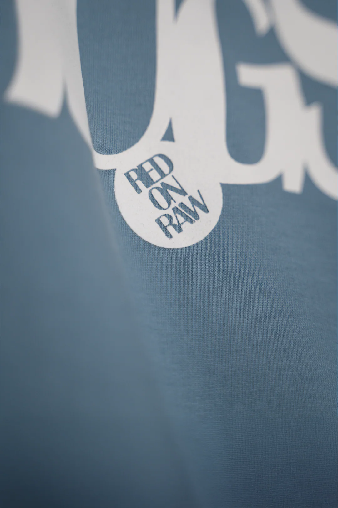 Light blue T-shirt close-up with RAW badge patch and printed lettering