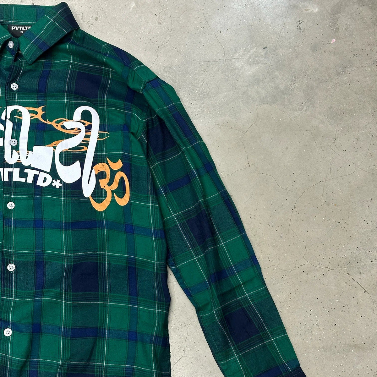 Green plaid long-sleeve button-up shirt angled view with white and gold lettering