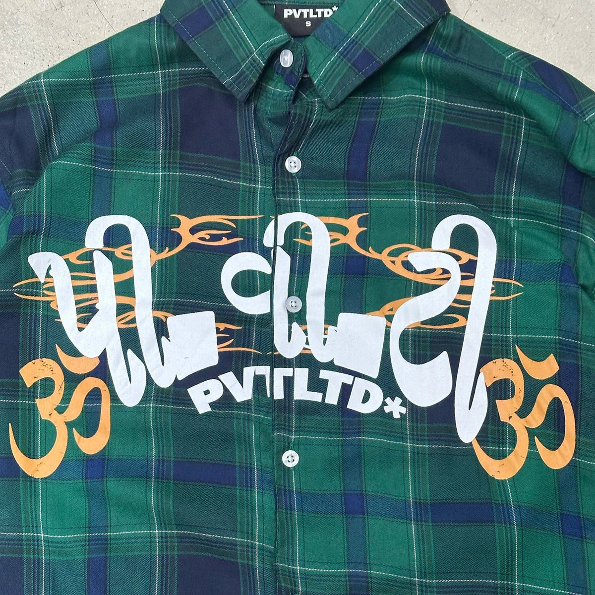 Green plaid button-up shirt close-up with white and gold front lettering graphic