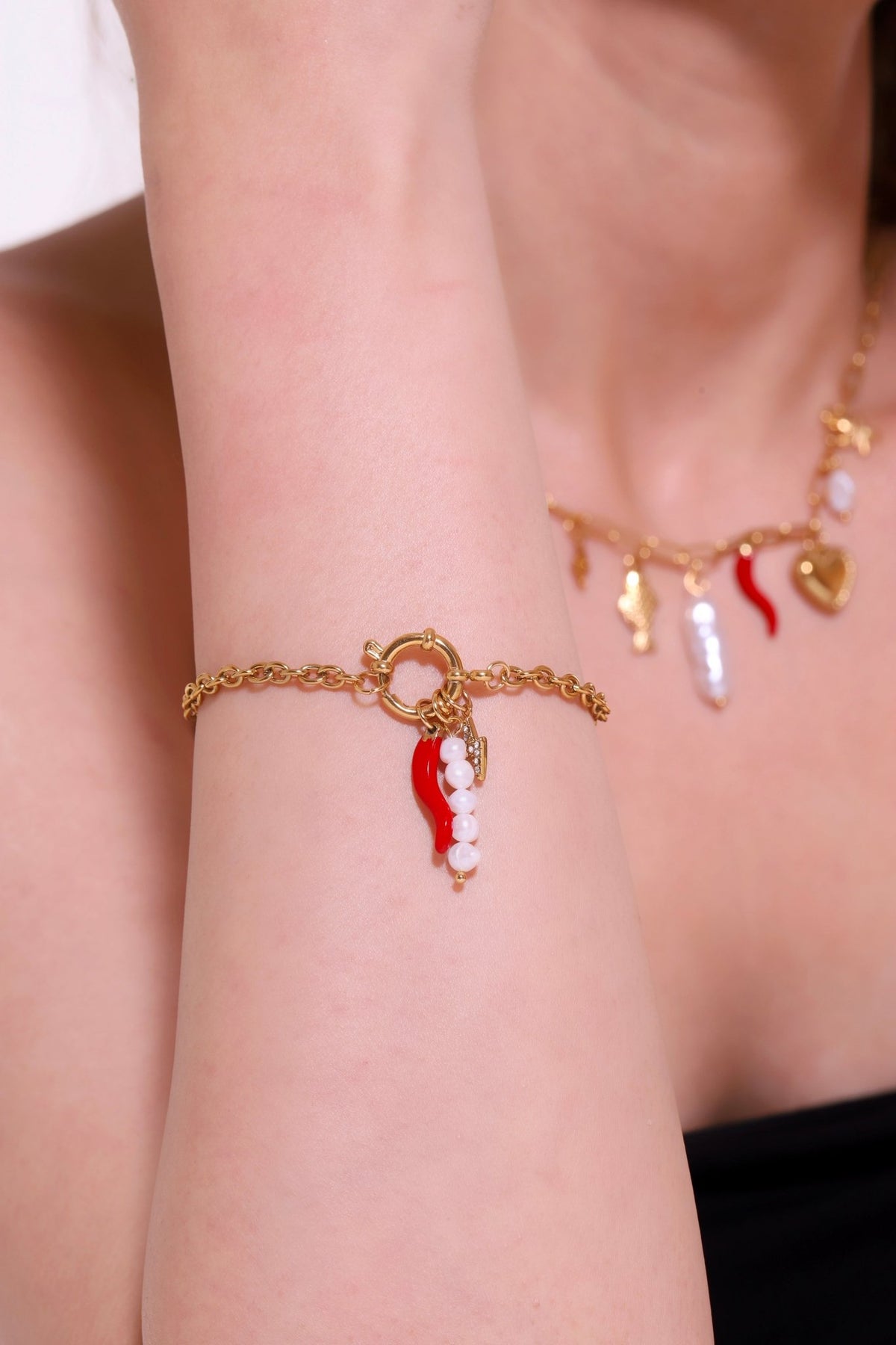 Gold charm bracelet on wrist with red chili pepper and pearl charms