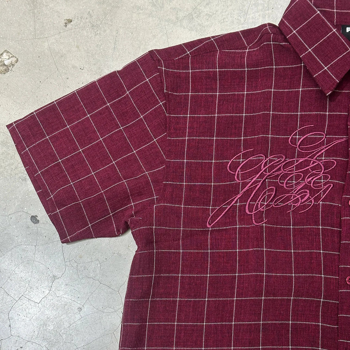 Burgundy plaid short-sleeve shirt with front script graphic, collar, and button placket