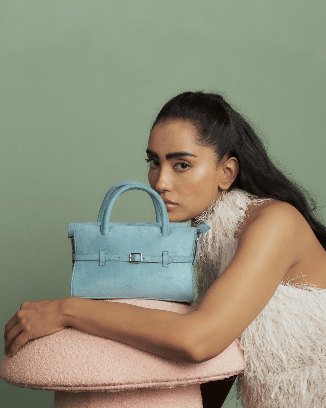 Powder blue mini handbag held by model, front buckle strap visible