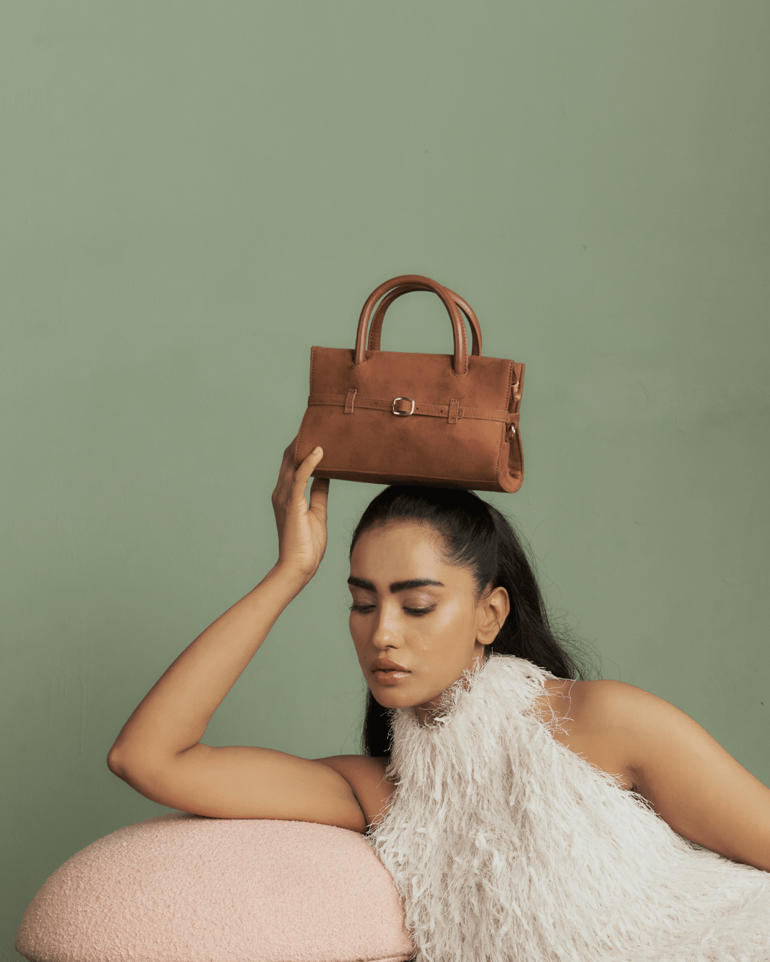 Tan mini handbag on model, showing top handles and front buckle strap.