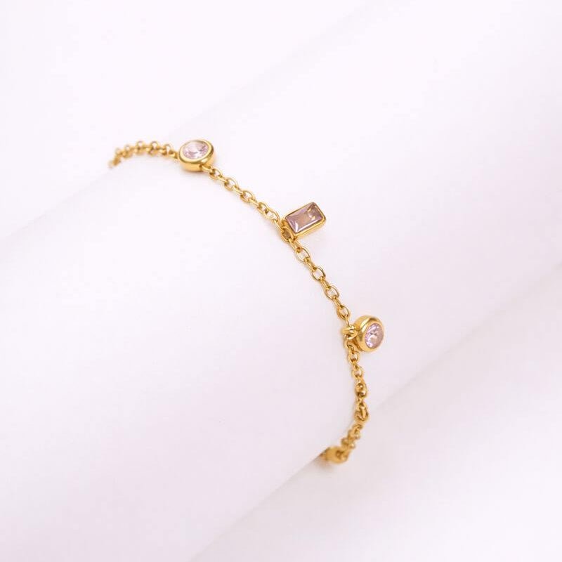 Gold-tone bracelet with pink round and square charm stones on linked chain.