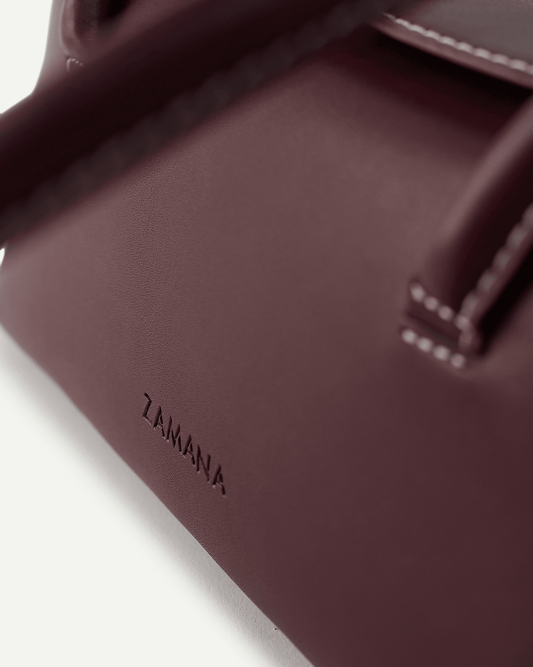 Close-up of burgundy bag base with embossed brand logo and trim stitching