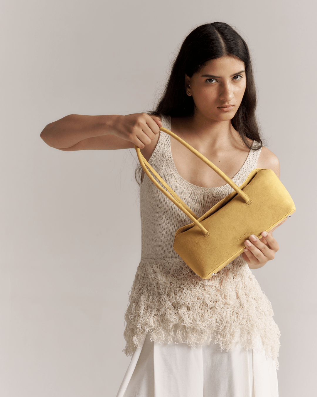 Mustard yellow suede tote bag with crossed handles, held in hand