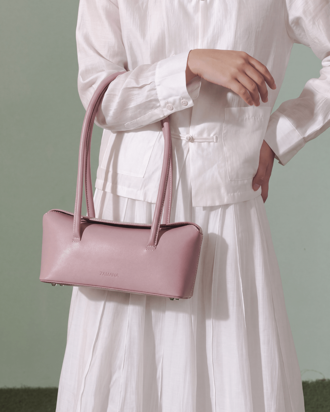 Pink handbag with dual top handles and stitched front, held at hip.