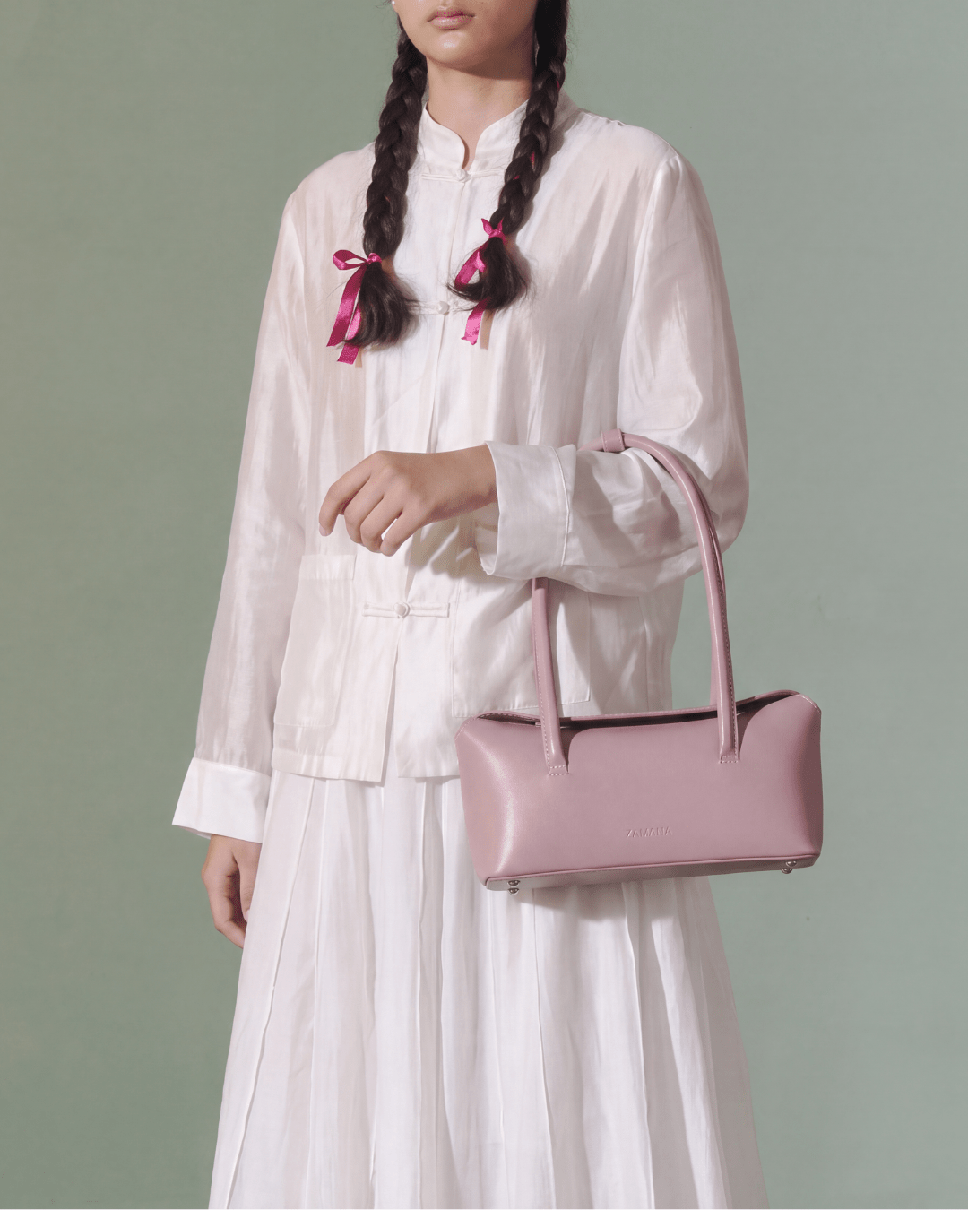Pink small handbag with two top handles, held across torso in side view.