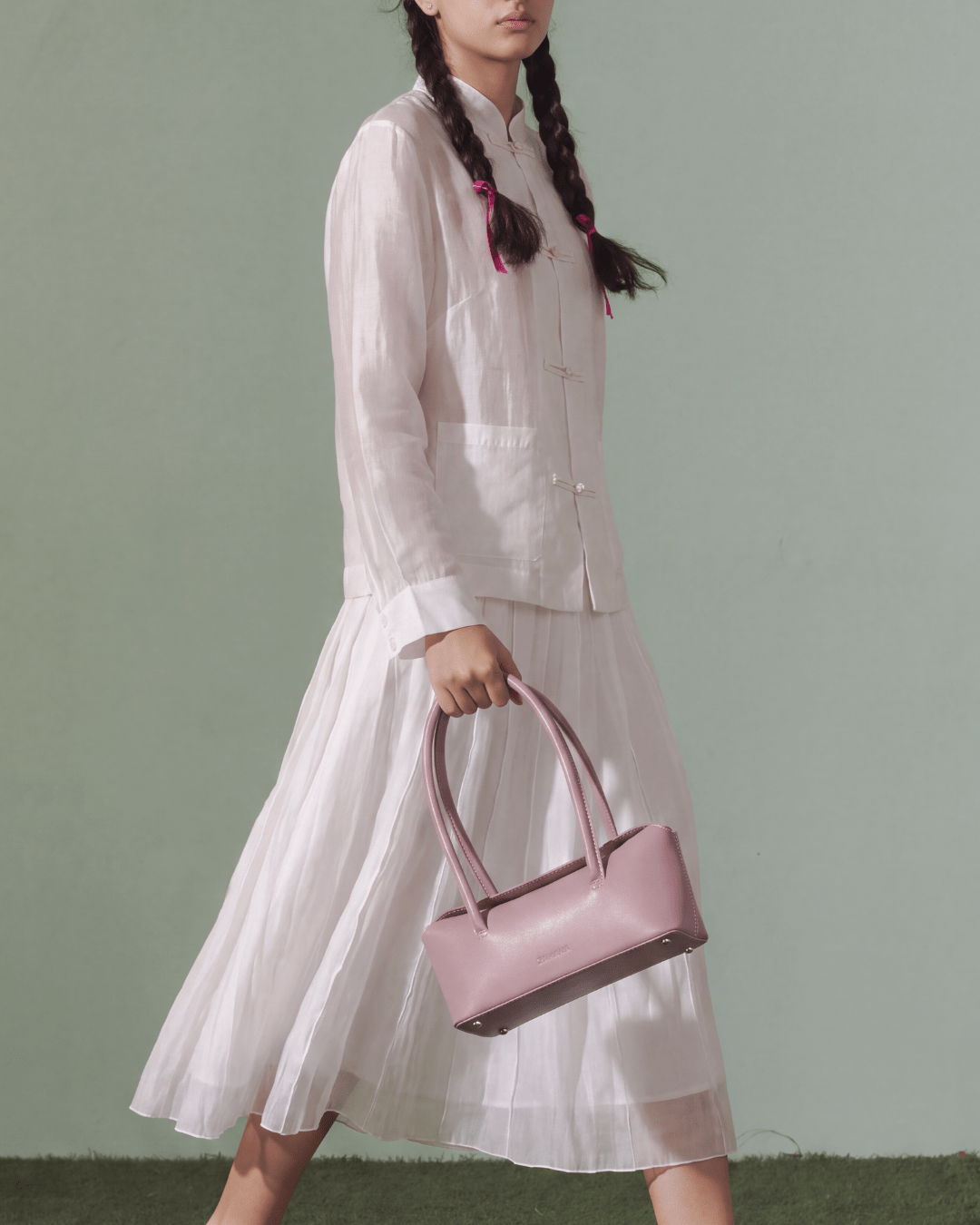 Pink small handbag with two top handles, held by model in front view.