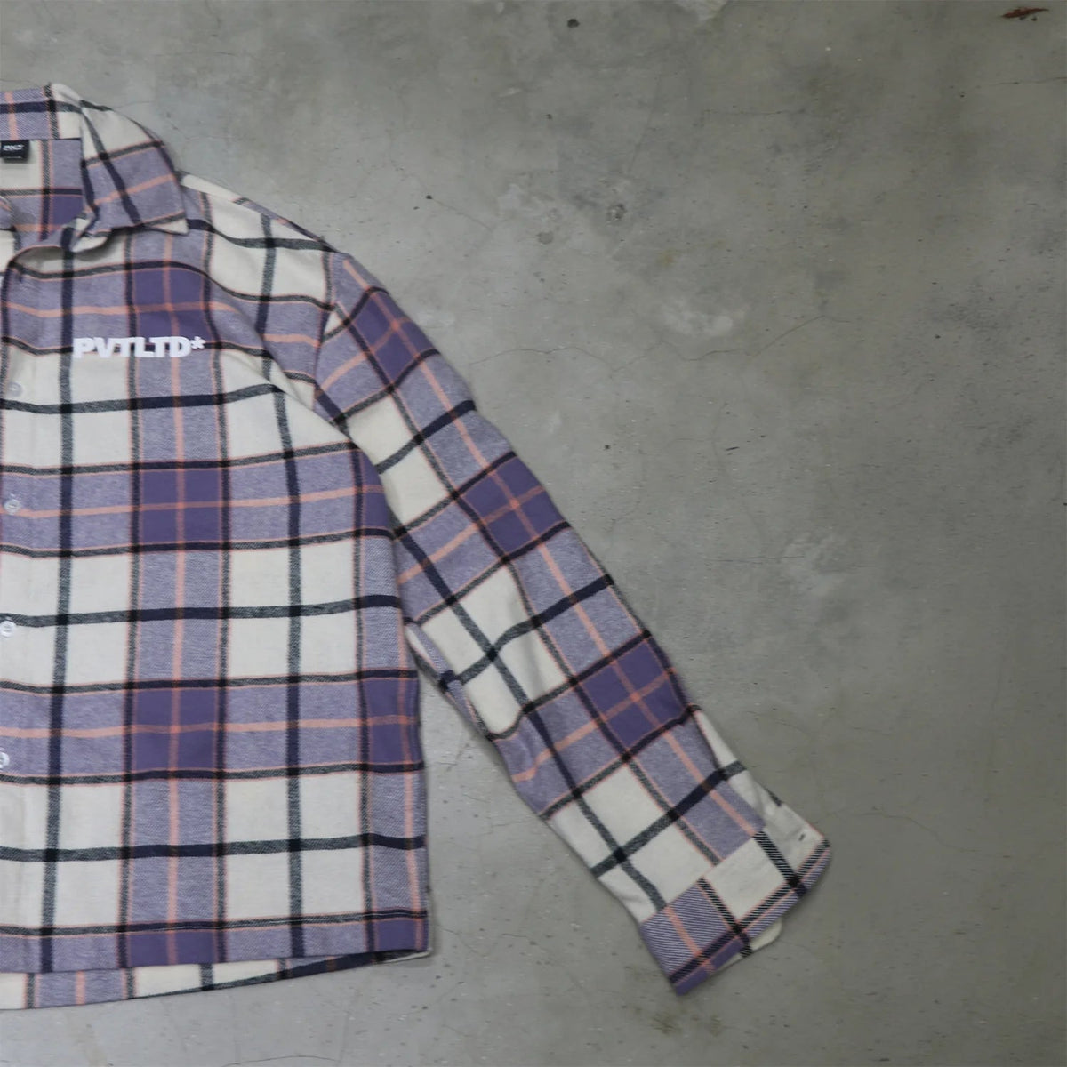 Side view of purple plaid button-up shirt with long sleeves and chest logo