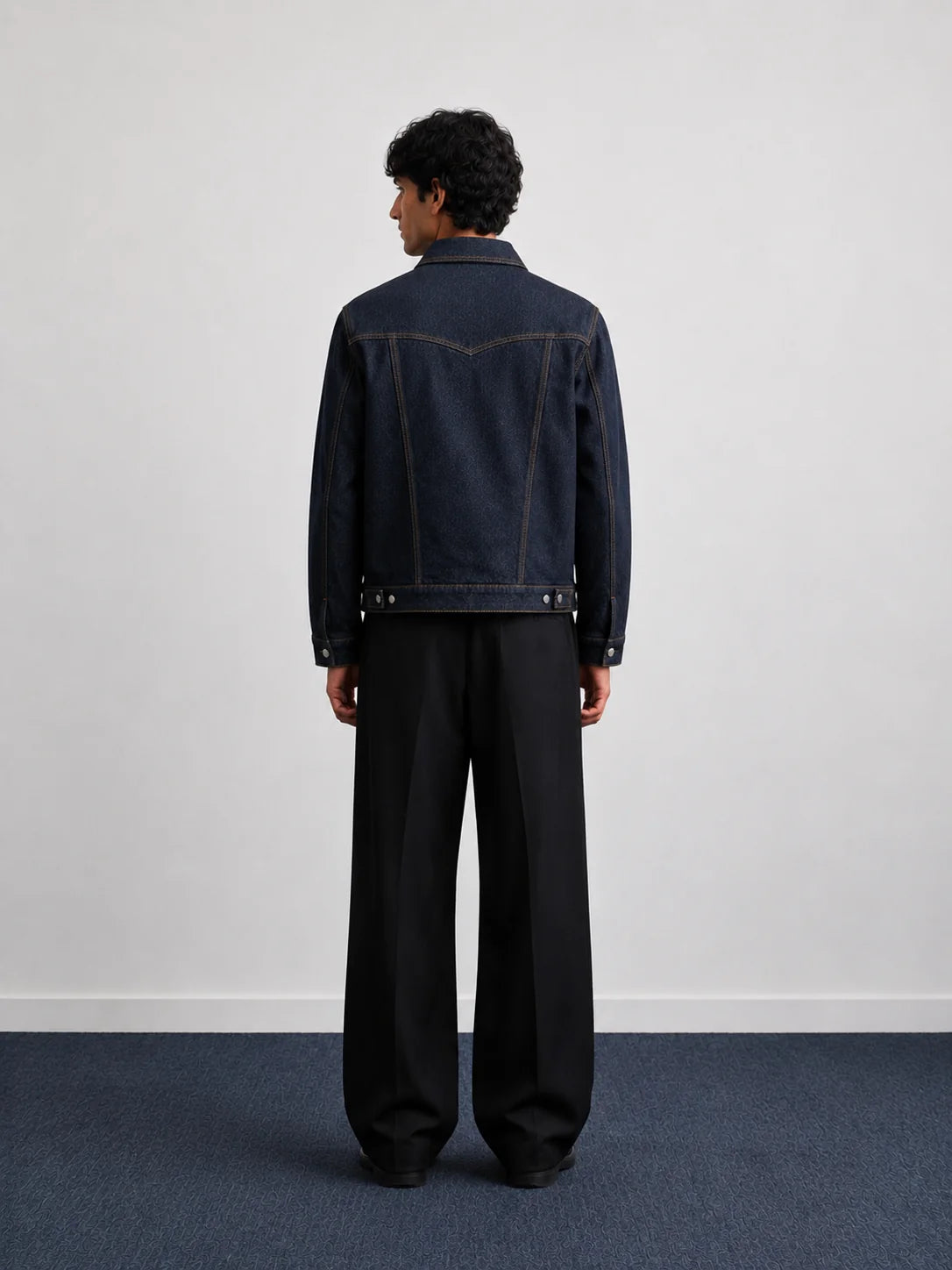 Indigo denim jacket back view with contrast stitching and buttoned hem, worn with trousers