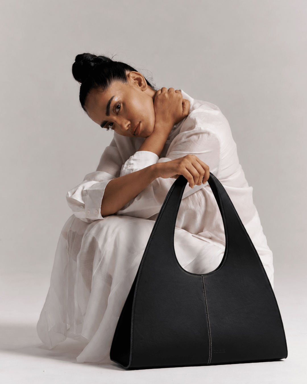 Black Sailor hobo bag held by model, oval cutout opening and center seam