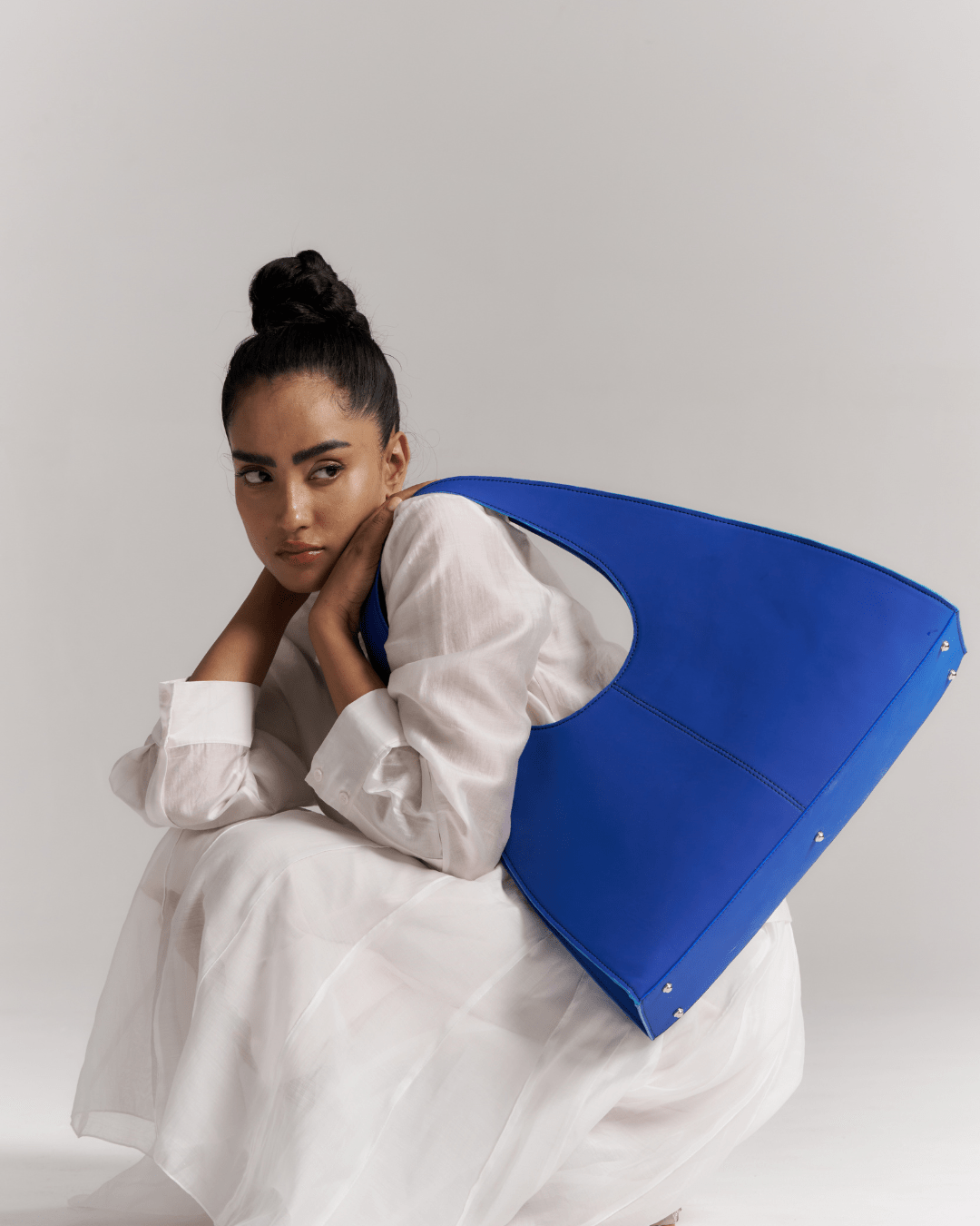 Blue triangular tote bag with oval handle opening, carried by model at an angle.