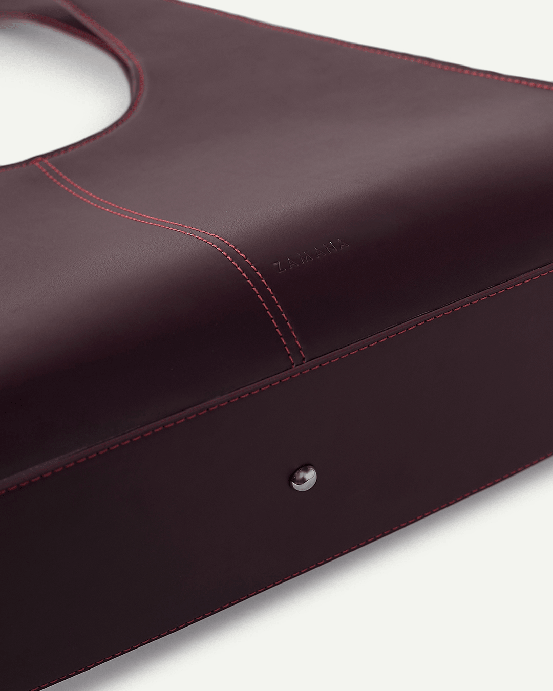 Burgundy leather tote bag close-up with red stitched seams and snap button