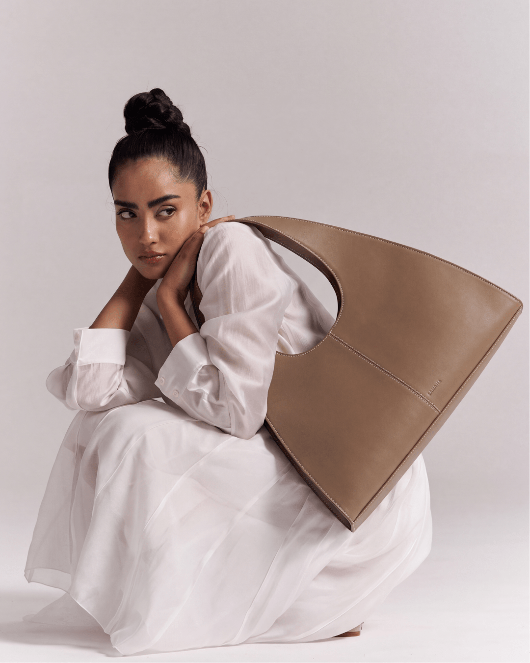 Caramel brown triangular handbag held by model, open oval top and short handles