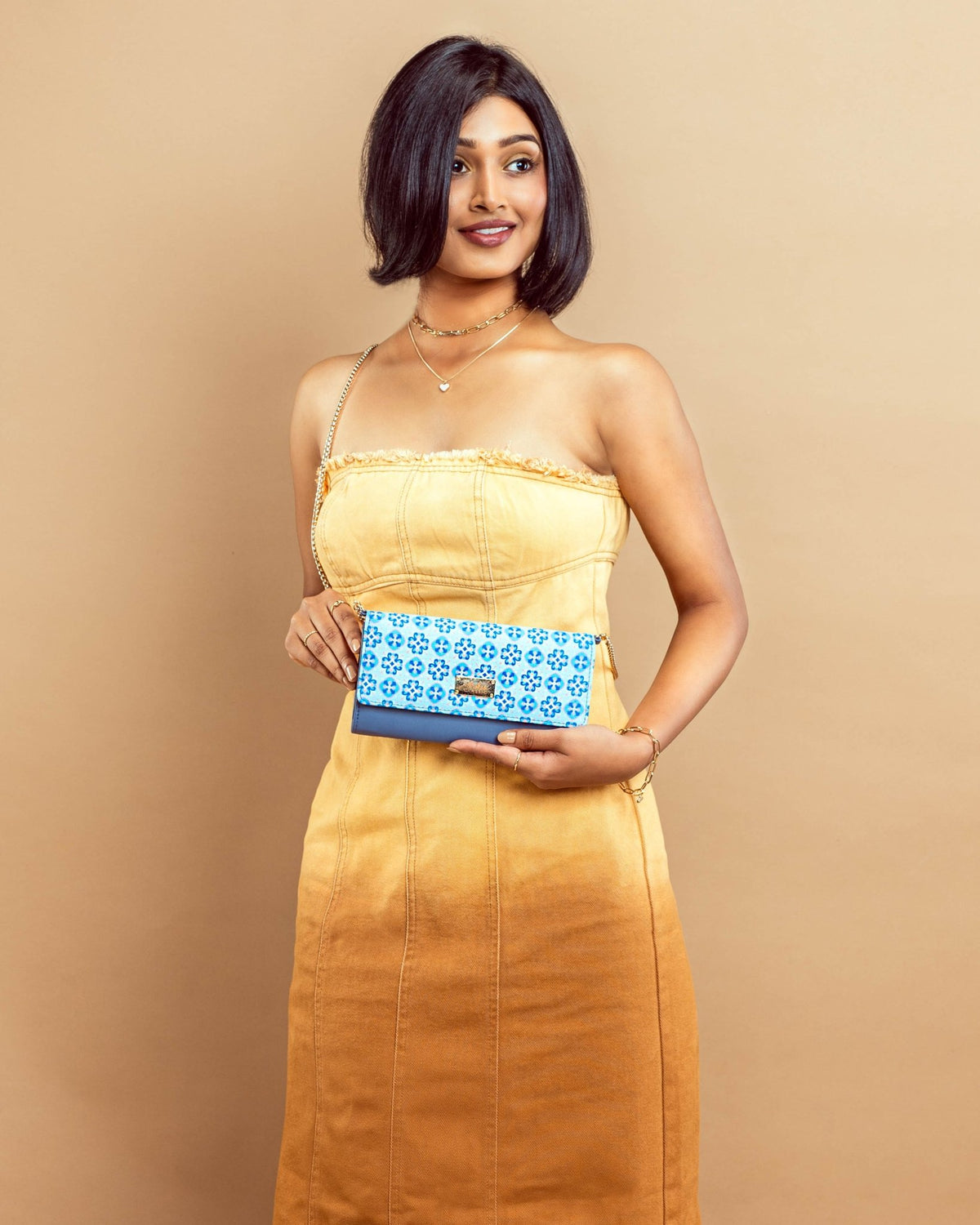 Blue floral clutch wallet with gold chain sling, held by a woman