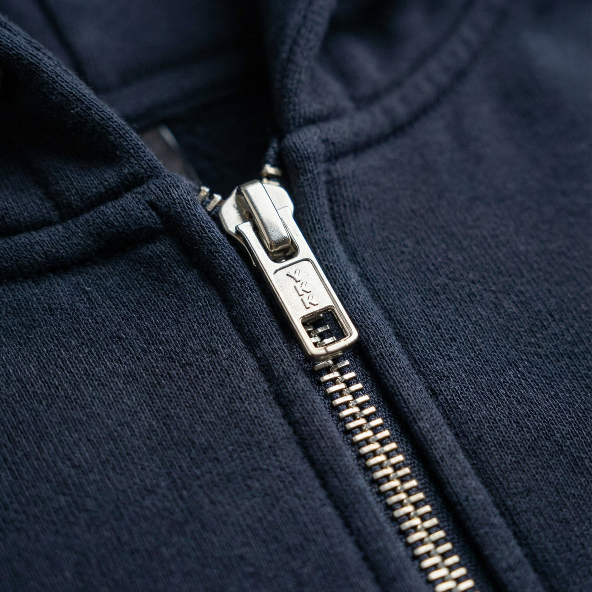 Navy hoodie close-up of front zipper with metal pull and ribbed collar