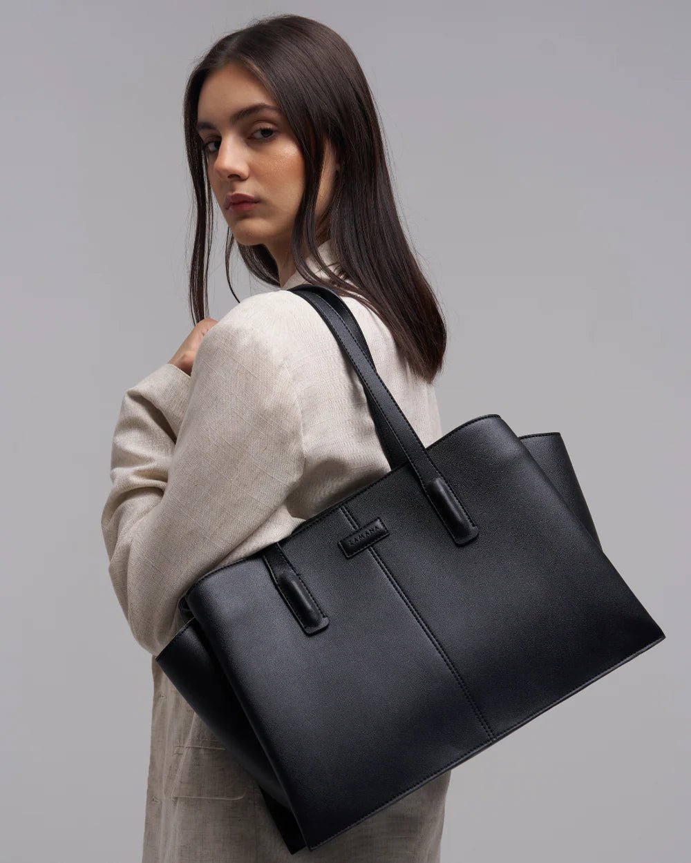Black tote bag with two top handles and front logo patch, structured rectangular shape.