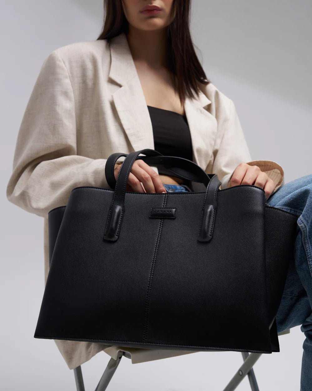 Black structured tote bag with front center seams and two top handles, close-up