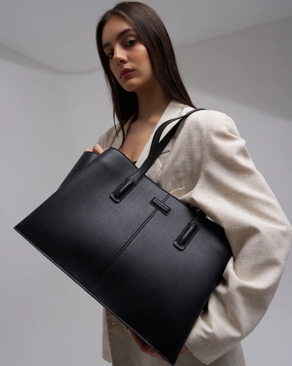 Black large tote bag with two top handles and front rectangular logo patch.